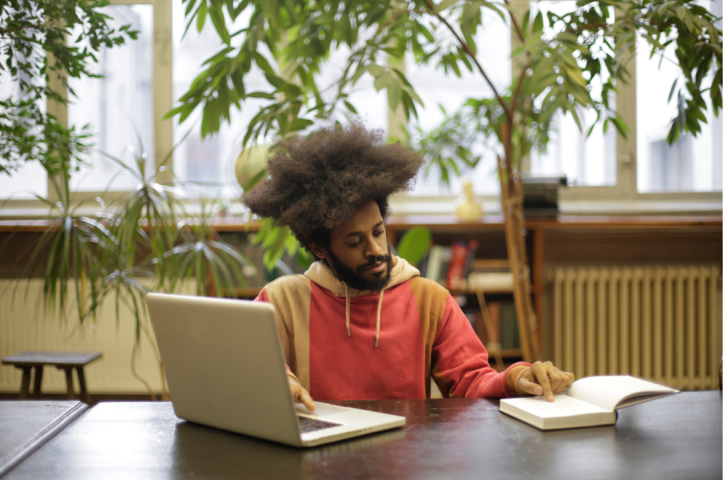 Mann recherchiert mithilfe eines Laptops und Buches